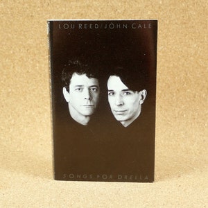 May include: A black and white photo of Lou Reed and John Cale on the cover of a cassette tape. The tape is titled "Songs for Drella".