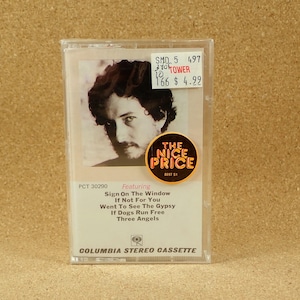 May include: A cassette tape case with a photo of a man with long brown hair. The case is white with black text that reads "PCT 30290 Featuring Sign On The Window If Not For You Went To See The Gypsy If Dogs Run Free Three Angels Columbia Stereo Cassette".
