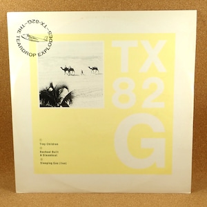 Può includere: Copertina dell'album "TX 82 G" di The Teardrop Explodes. La copertina presenta una scena del deserto in bianco e nero con cammelli e palme, su uno sfondo giallo con un grande testo bianco. Il titolo dell'album e la lista dei brani sono visibili.