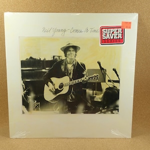 Puede incluir: Portada de álbum de vinilo con una imagen en tonos sepia de Neil Young tocando una guitarra acústica en el escenario. El álbum se titula "Comes A Time" y tiene una pegatina de "Super Saver Series".