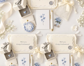May include: A bridesmaid proposal gift set featuring a cream canvas pouch with a Will you be my bridesmaid card, a heart-shaped necklace in a gift box, a blue floral compact mirror, a floral note card, a gold pen, and a sheer organza bag.
