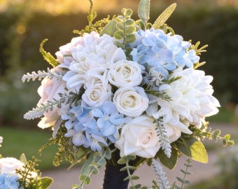 Könnte beinhalten: Ein Blumenstrauß mit weißen Rosen, weißen Dahlien und hellblauen Hortensienblüten. Das Arrangement enthält grüne Eukalyptusblätter und silberfarbenes Blattwerk, die mit einem dunkelblauen Band um die Stiele zusammengebunden sind.