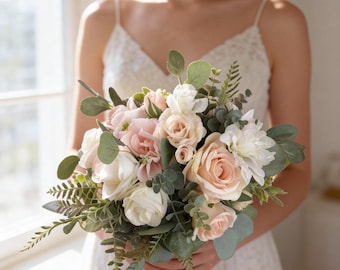 Könnte beinhalten: Ein Brautstrauß mit weißen und pfirsichfarbenen Rosen, Dahlien und Grünzeug. Der Strauß ist mit einem pfirsichfarbenen Satinband gebunden. Die Blumen haben verschiedene Texturen und Formen.