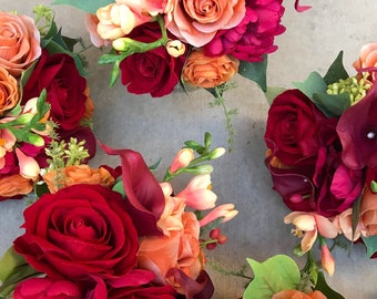 Könnte beinhalten: Eine Ansammlung von vier Blumensträußen mit dunkelroten, leuchtend orangen und zart pfirsichfarbenen Rosen, dunkelburgunderfarbenen Calla-Lilien und kleinen gelben Freesienknospen. Jedes Arrangement enthält grünes Blattwerk und kleine Beerenakzente.