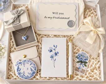 May include: A gift box containing a heart-shaped pendant necklace, a small mirror with blue floral patterns, a notebook with a blue flower illustration, a white pen, a pouch, and a card with the text Will you be my bridesmaid.