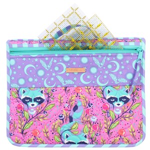 May include: A purple and pink quilted zippered pouch with a raccoon print and a zippered pocket on the top. The pouch has a teal zipper and a blue and white striped border. The pouch is filled with clear plastic rulers.