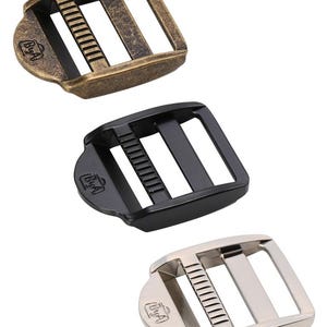 May include: Three metal slider buckles in antique brass, black, and silver finishes. Each buckle has a rectangular shape with two slots and a small logo on the side.