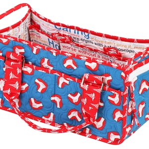 May include: A blue and red quilted tote bag with a zipped pocket and multiple pockets on the front. The bag has a red handle and is decorated with a white print of a heart with a caduceus symbol. The bag is lined with a white fabric with text that reads "Nurses are angels with a stethoscope. If love can't cure it, nurses can't cure it. We'd be worse without a nurse."