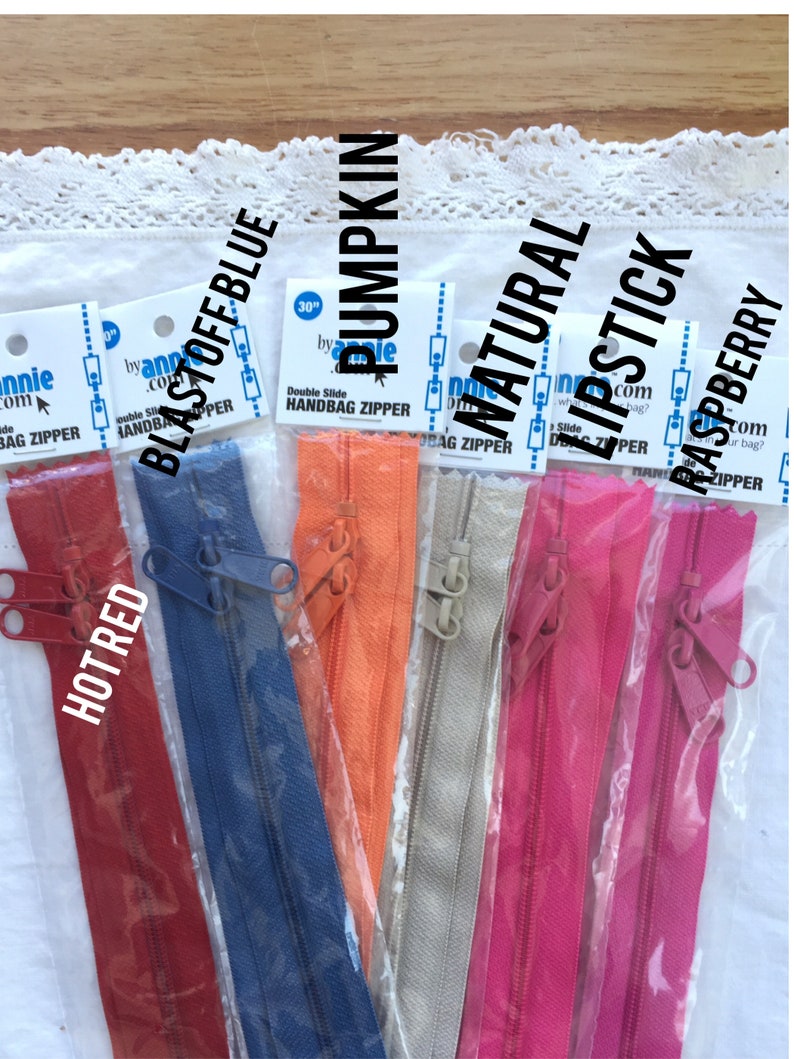 May include: Assortment of 30-inch double slide handbag zippers in various colors, including hot red, blast off blue, pumpkin, natural, lipstick, and raspberry.