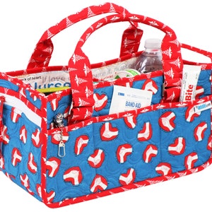 May include: Red and blue quilted tote bag with a zipped pocket and multiple compartments. The bag is decorated with a pattern of red hearts and medical caduceus symbols. The bag is filled with various medical supplies, including a bottle of water, a roll of bandages, and a tube of ointment. The bag has a label that says "Bite" and a website address.