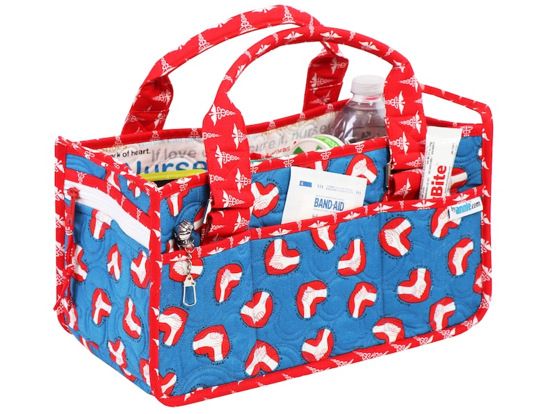 May include: Red and blue quilted tote bag with a zipped pocket and multiple compartments. The bag is decorated with a pattern of red hearts and medical caduceus symbols. The bag is filled with various medical supplies, including a bottle of water, a roll of bandages, and a tube of ointment. The bag has a label that says "Bite" and a website address.