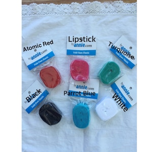 May include: Six spools of fold-over elastic in various colors: atomic red, lipstick, turquoise, black, parrot blue, and white. Each spool is labeled with the color name and "by annie.com".