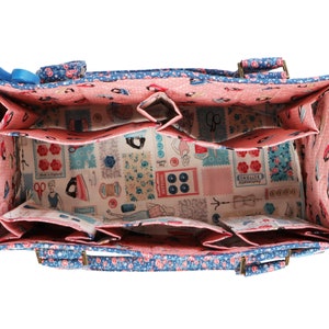 May include: A blue and pink fabric tote bag with multiple compartments and two handles. The bag is lined with a pink fabric and has a floral print.