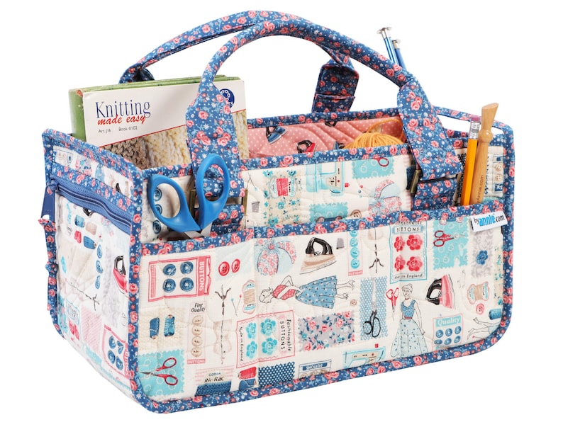 May include: A blue and white fabric tote bag with multiple pockets and compartments. The bag has a floral pattern and features a variety of sewing-themed images, including buttons, scissors, and an iron. The bag is filled with various sewing supplies, including yarn, needles, and scissors.