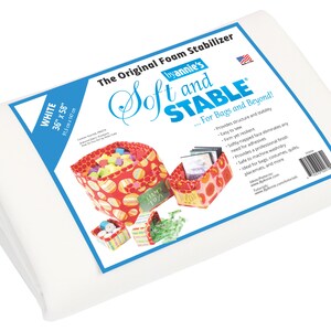 May include: White foam stabiliser sheet, 36 inches by 58 inches, by Annie's Soft and Stable, for bags and beyond. The product is shown folded in half. The packaging shows a red, white, and green patterned bag with a variety of items inside.