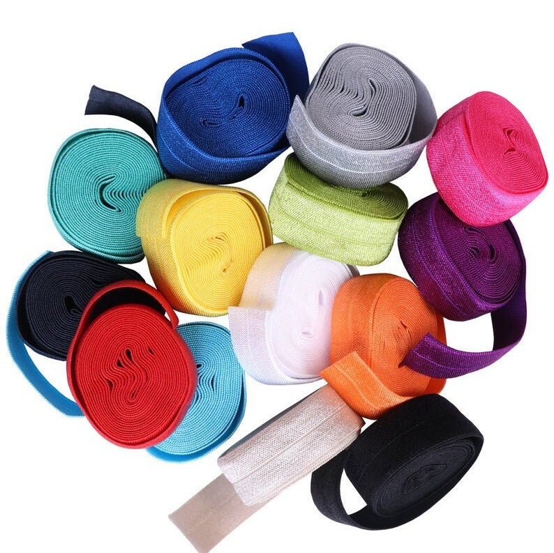 May include: Assortment of colorful elastic bands in various colors, including black, white, red, orange, yellow, green, blue, purple, and pink. The elastic bands are rolled up and arranged in a circle.
