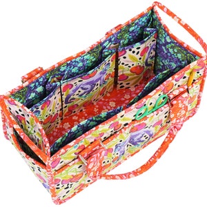 May include: A colourful fabric tote bag with multiple pockets and a zipper closure. The bag is lined with a floral print fabric and has a cherry pattern on the outside.