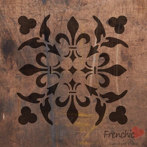 May include: Black and white stencil featuring a repeating pattern of fleur-de-lis and quatrefoil designs. The stencil is on a brown wooden surface. Frenchic Furniture Paint.
