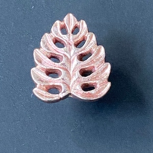 Pode incluir: Um botão de armário em forma de folha de cor cobre com um design recortado.