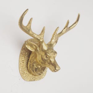 May include: A brass deer head wall mount with detailed antlers and a textured surface. The deer head is mounted on an oval-shaped plaque. The sculpture is a decorative item.