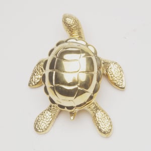 May include: A golden turtle figurine with detailed shell and flipper textures. The turtle's head and limbs are extended, giving it a lifelike appearance. The figurine is made of a shiny, reflective material.