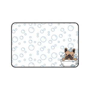 May include: A rectangular desk mat featuring a white background with a pattern of light blue outlined bubbles. In the bottom right corner, a tan French Bulldog with a black nose and ears is sitting in a white bathtub filled with blue bubbles.