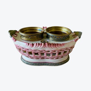 May include: A white ceramic double-sided dish with pink accents and a woven design. The dish has two brass bowls with decorative edges.