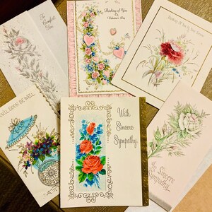 May include: A collection of vintage greeting cards with floral designs. The cards feature roses, carnations, and other flowers in various colors, including pink, red, and blue. Some cards have gold accents and text such as "Thinking of You" and "With Sincere Sympathy."