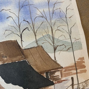 May include: Watercolor painting of a winter landscape featuring a barn with brown and black roofs. Bare trees stand against a blue and white sky, with a hint of mountains in the background. The artwork evokes a serene, rural scene.