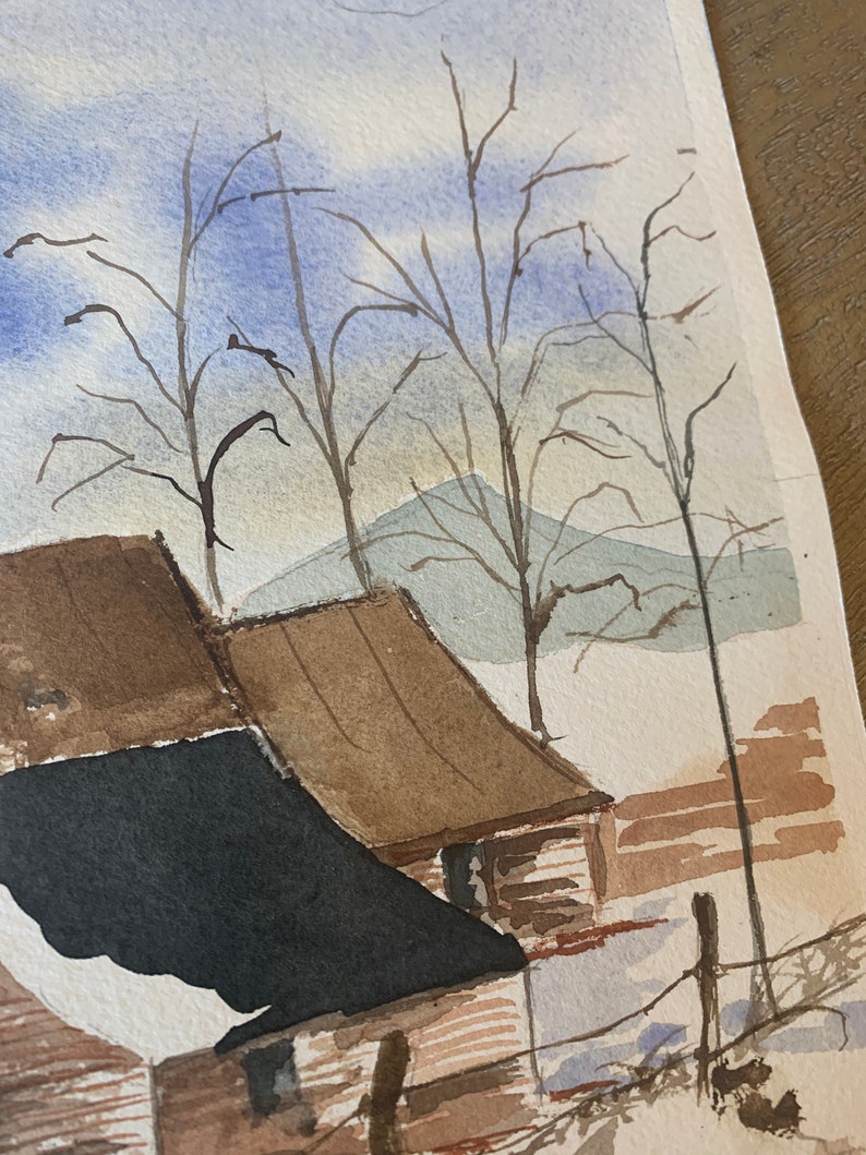 May include: Watercolor painting of a winter landscape featuring a barn with brown and black roofs. Bare trees stand against a blue and white sky, with a hint of mountains in the background. The artwork evokes a serene, rural scene.