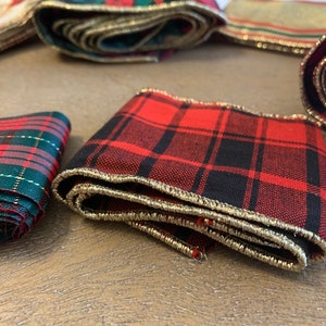 May include: Red and black plaid ribbon with gold trim. The ribbon is folded and has a textured surface.