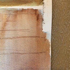 May include: Watercolor painting with a textured, layered effect. The artwork features shades of brown and tan, with visible brushstrokes and a rough, unfinished edge. The painting's composition is abstract, with horizontal lines and a blend of colors.