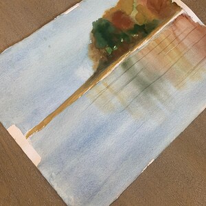 May include: Watercolor painting of a landscape with a tree and water. The tree is painted with shades of green, brown, and yellow. The water is painted with shades of blue and white. The painting is on a white paper.