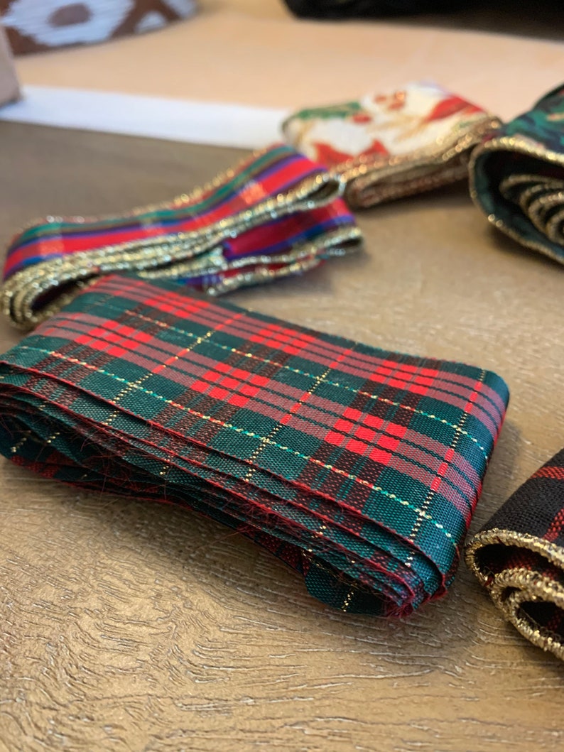 May include: A close-up of a red and green plaid ribbon with gold trim. The ribbon is folded and stacked on a wooden surface.