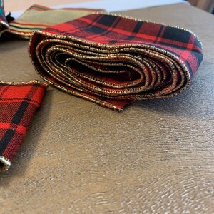 May include: Red and black plaid ribbon with gold trim. The ribbon is rolled up and has a gold edge.