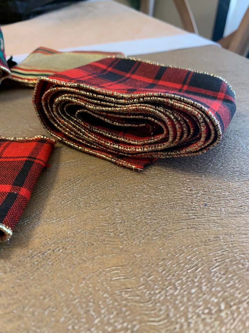 May include: Red and black plaid ribbon with gold trim. The ribbon is rolled up and has a gold edge.