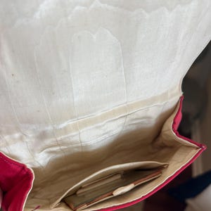 K&ouml;nnte beinhalten: Eine rote Clutch aus Satin mit einem wei&szlig;en Satin-Innenfutter. Die Clutch hat eine kleine Tasche im Inneren.