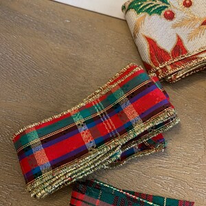 May include: Two rolls of red and green plaid ribbon with gold trim. The ribbon is folded and stacked on a wooden surface.