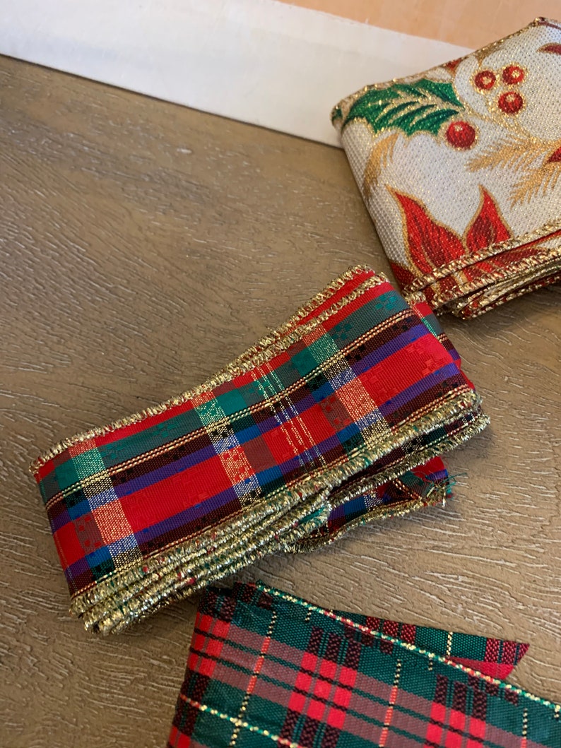 May include: Two rolls of red and green plaid ribbon with gold trim. The ribbon is folded and stacked on a wooden surface.