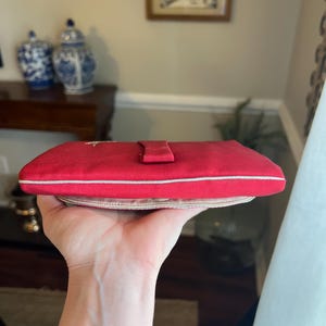 K&ouml;nnte beinhalten: Eine rote Clutch aus Satin mit wei&szlig;em Besatz und einem kleinen Klappverschluss.