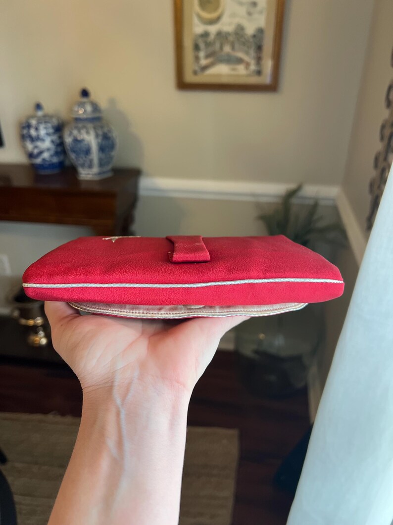 K&ouml;nnte beinhalten: Eine rote Clutch aus Satin mit wei&szlig;em Besatz und einem kleinen Klappverschluss.
