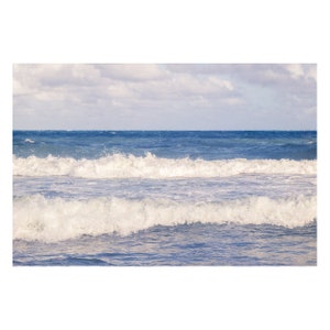 May include: A close-up of ocean waves crashing on the shore. The water is a deep blue, and the waves are white and foamy. The sky is cloudy and light blue.