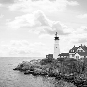 May include: A black and white photograph of a lighthouse on a rocky cliff overlooking the ocean. The lighthouse is tall and white with a black top. The sky is cloudy and the water is choppy.