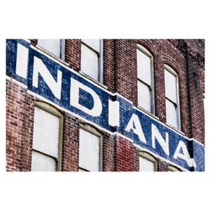 May include: A brick building with a large sign that reads "INDIANA" in white letters with a blue outline. The sign is painted on the side of the building and is angled upwards.
