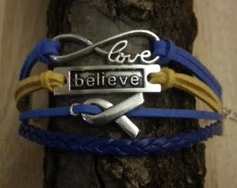 May include: Multi-layered bracelet with blue and yellow leather straps, featuring a silver infinity symbol with the word "love" inscribed, a silver charm with the word "believe" and a silver ribbon charm.
