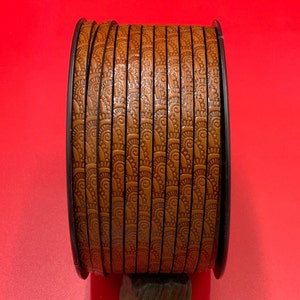 May include: A roll of brown leather cord with a decorative embossed pattern. The cord is wound around a black spool.