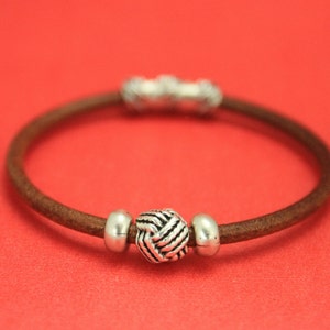 May include: A brown leather bracelet with a silver knot-shaped bead and two silver spacer beads.