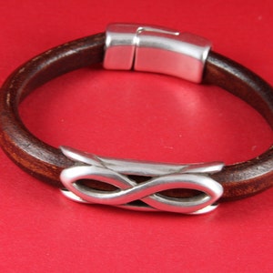 May include: A brown leather bracelet with a silver infinity symbol charm and a silver magnetic clasp.