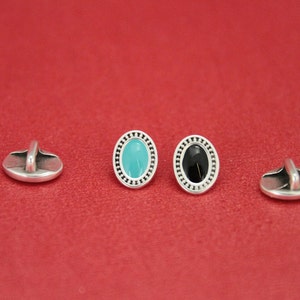 May include: Three silver oval buttons with a decorative border. One button has a turquoise center, one has a black center, and one is plain.