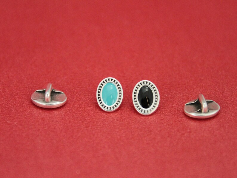 May include: Three silver oval buttons with a decorative border. One button has a turquoise center, one has a black center, and one is plain.